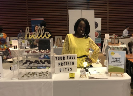 Janelle smiling at a table displaying her various protein bites.