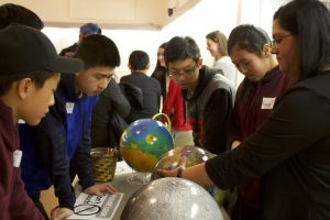 Group of students surrounding table with Dr. Shankar teaching and referring to globes on a table.