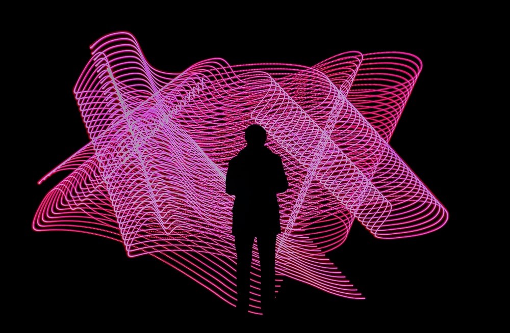 A silhouetted figure standing in front of a large art piece with magenta interlaced stacked lines