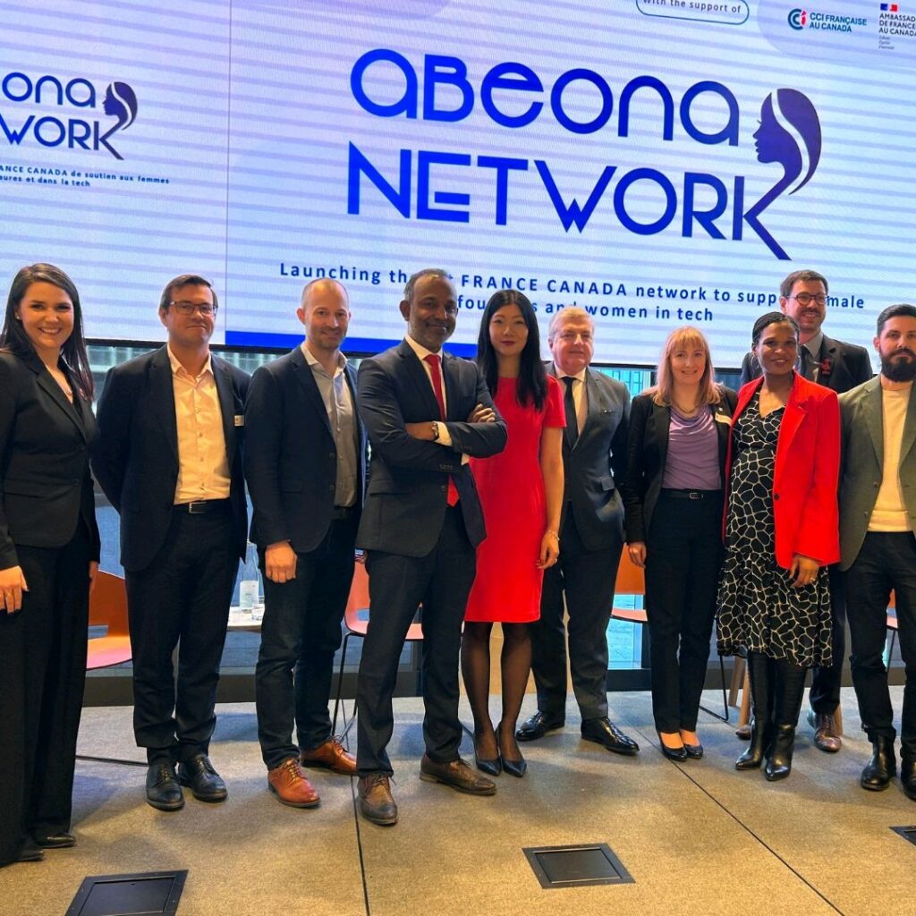 Ten people standing in line, smiling and posing for a photo in front of a large screen that reads "Abeona Network"