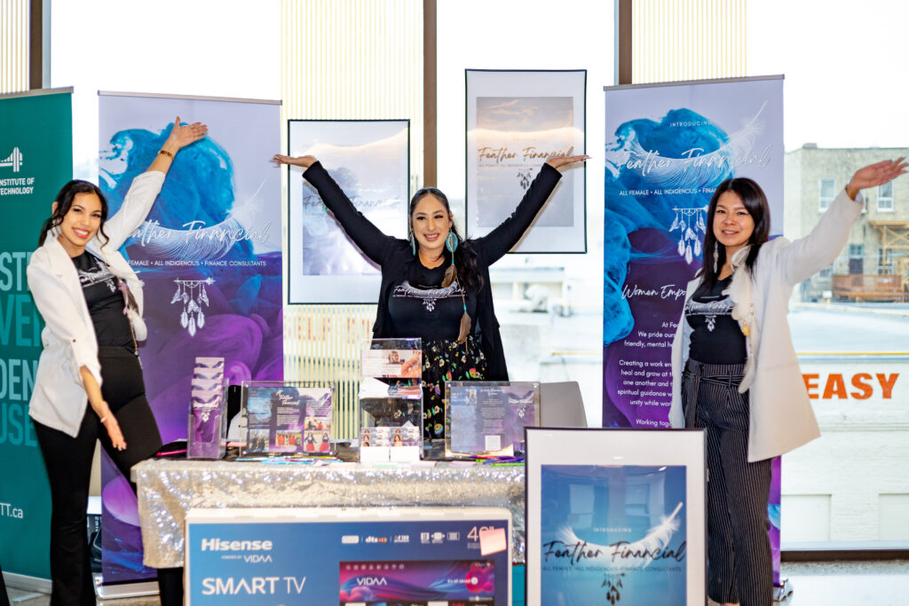 Three women smiling and standing at a booth with their products.