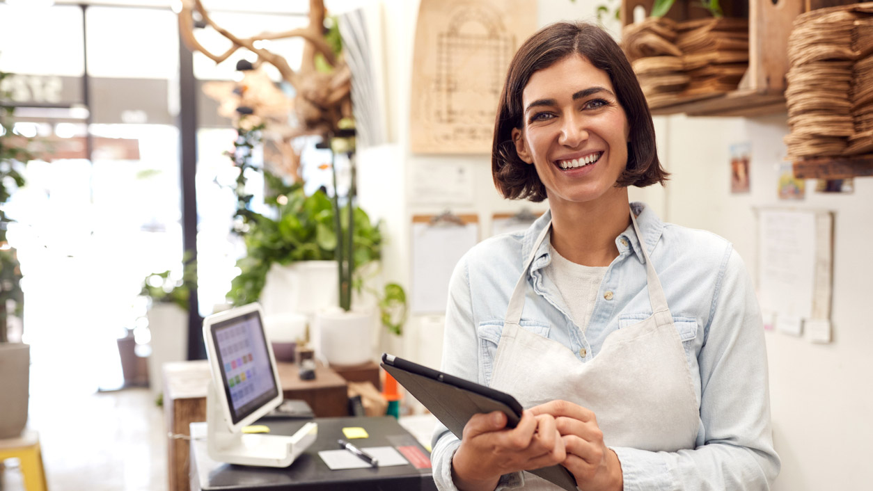 Portrait Of Female Owner With Digital Tablet Standing Behind Sales Desk Of Florists Store