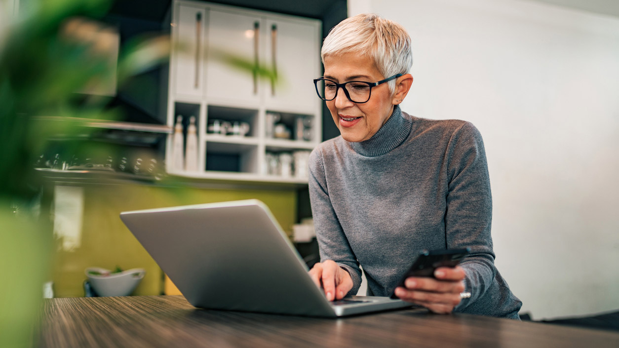 Modern mature woman using laptop and smart phone at home, portrait